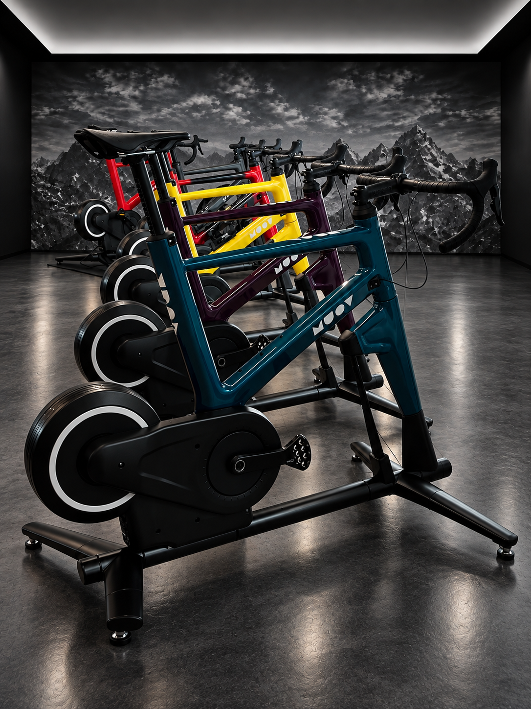 A row of MUOV bikes in teal, plum, yellow and red finishes in a dark studio with a monochrome mountain backdrop