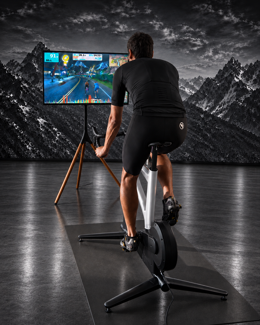Rider on a white MUOV bike facing a screen running a virtual cycling world, mountain backdrop behind