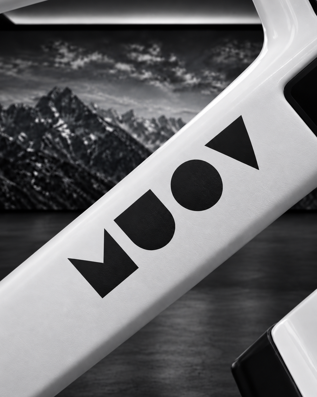 Close-up of the MUOV logo on a white bike frame with a monochrome mountain backdrop behind